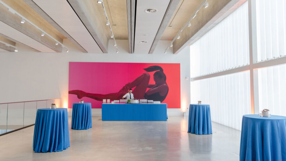 A large event space in London, a bright gallery with poser tables, a bar and a large print of a ballet dancer in the background.