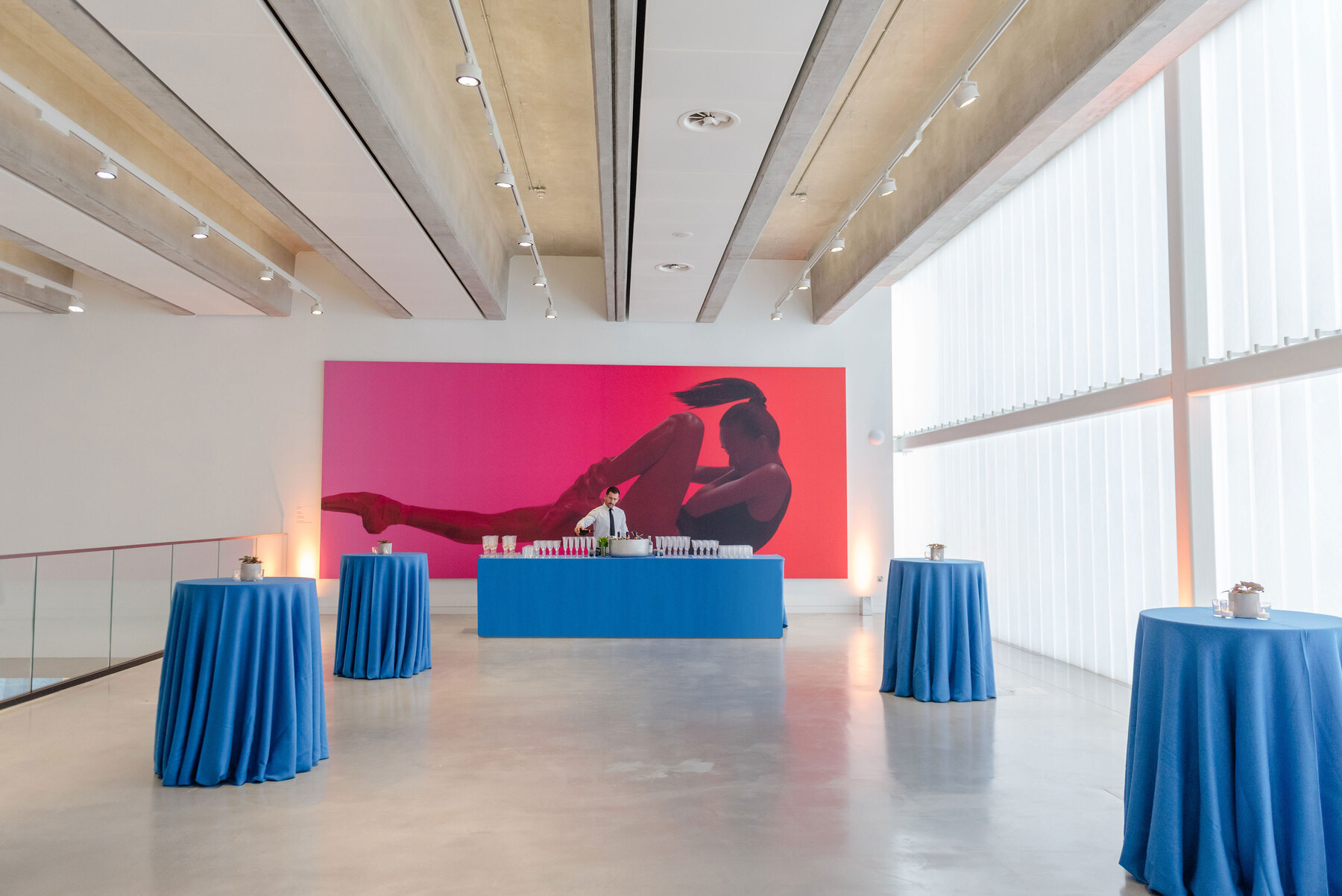 A large event space in London, a bright gallery with poser tables, a bar and a large print of a ballet dancer in the background.