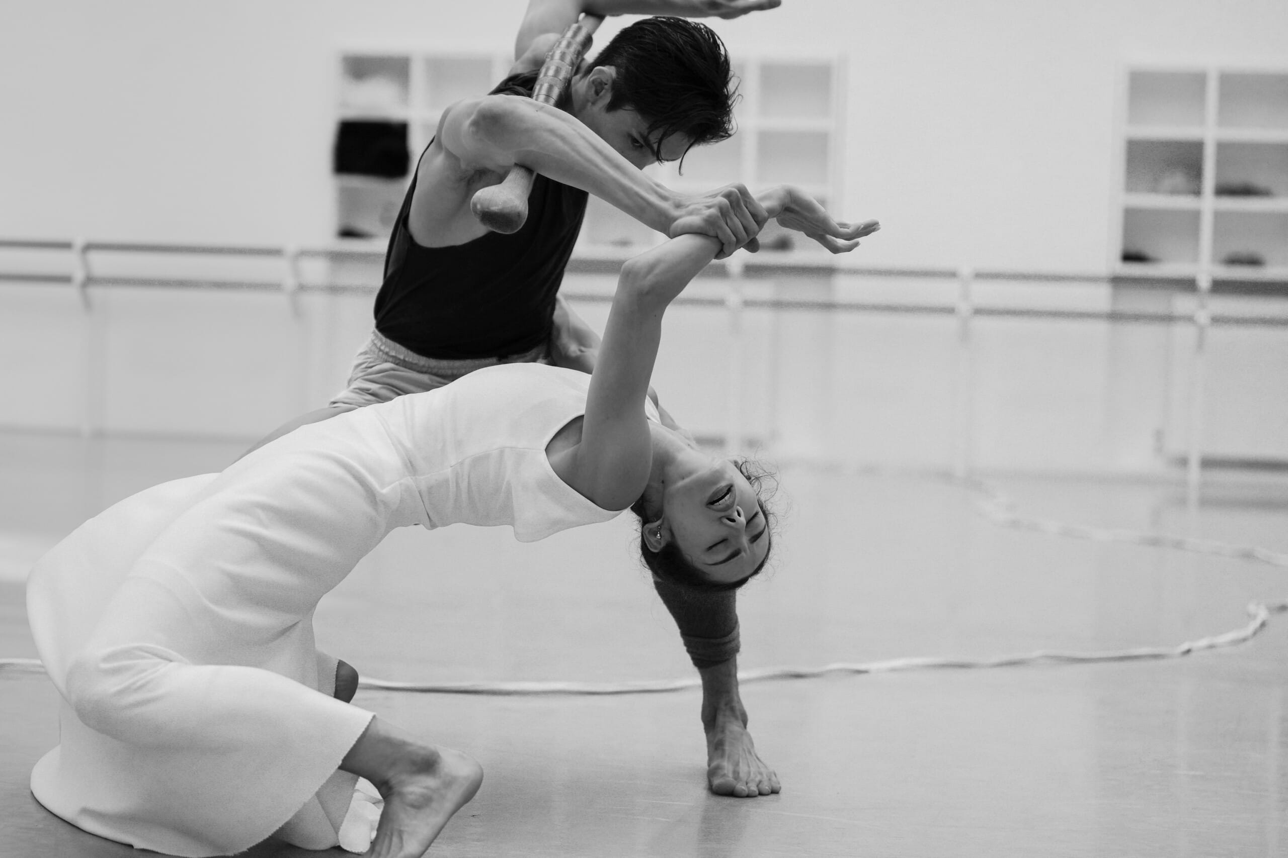 Two dancers perform a contemporary duet in a studio. The dancer in front