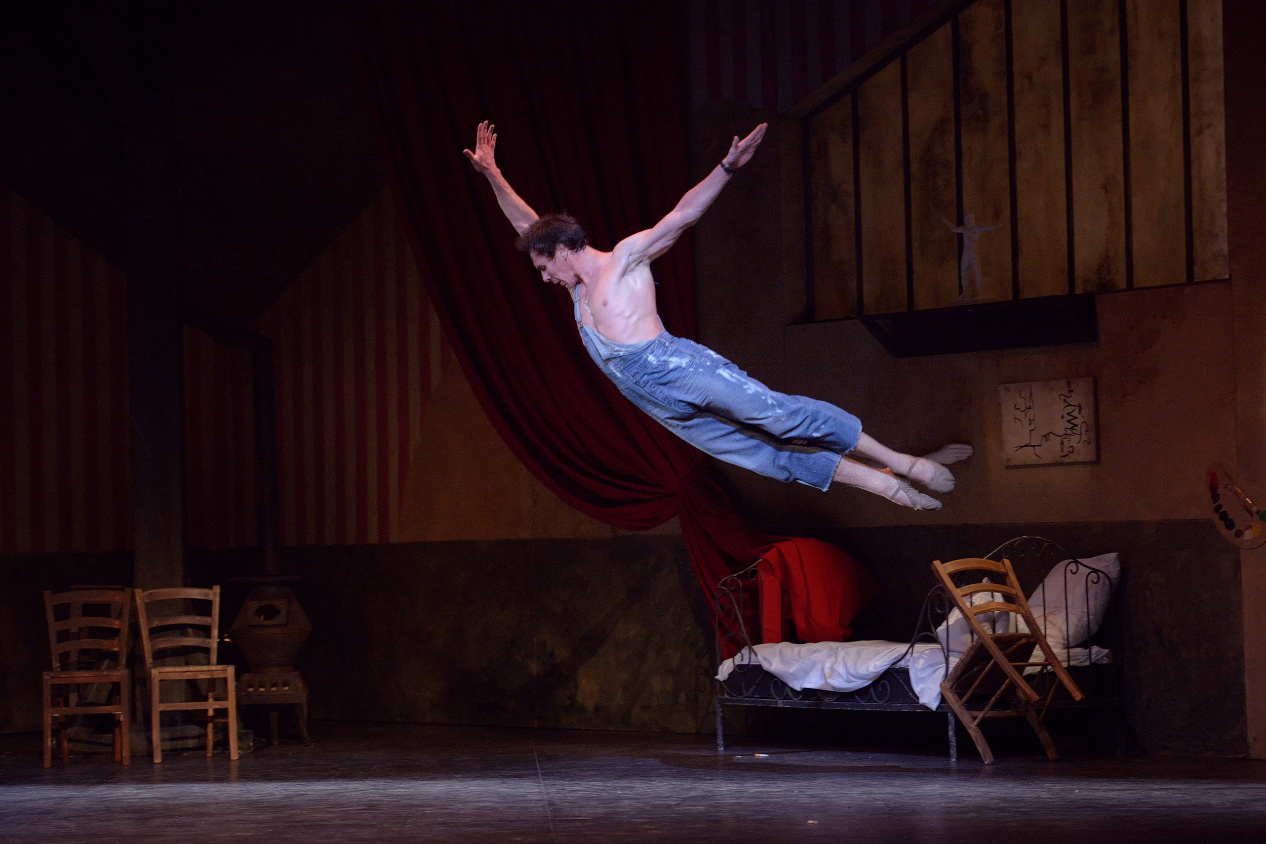 Male ballet dancer in mid-air performing an athletic leap in overalls