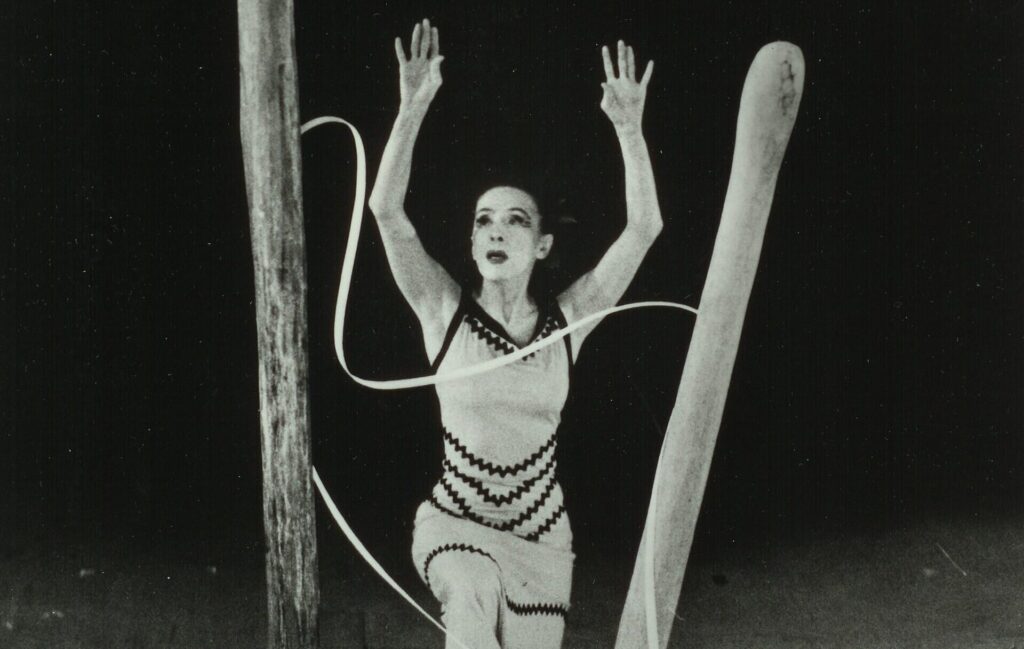 A dancer performs on stage surrounded by large wooden structures and long