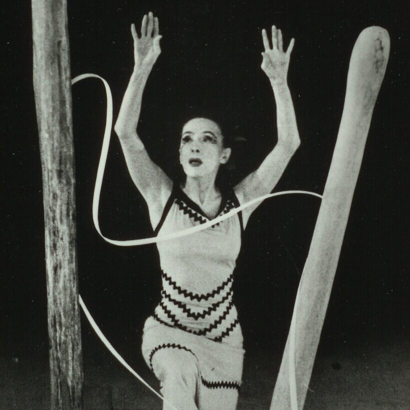 A dancer performs on stage surrounded by large wooden structures and long