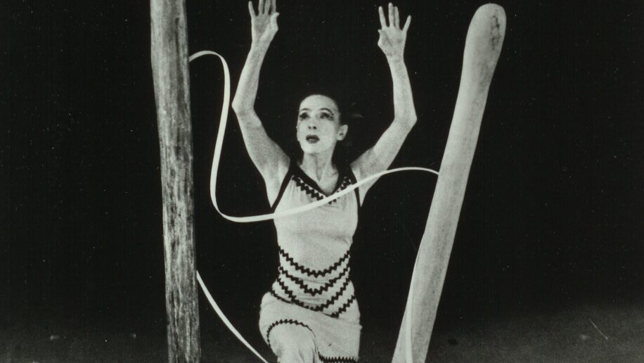 A dancer performs on stage surrounded by large wooden structures and long
