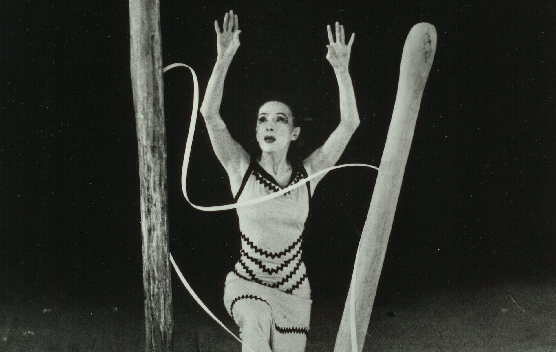 A dancer performs on stage surrounded by large wooden structures and long